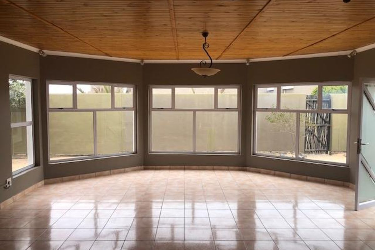 Spacious sunroom featuring large windows, tiled flooring, and a distinctive timber-paneled vaulted ceiling, offering a bright and versatile living space.