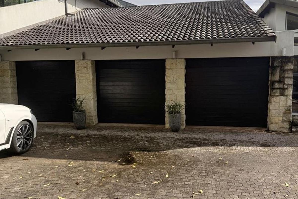 A triple garage featuring dark modern doors, stone-clad support pillars, and a tiled roof, set against a paved driveway.