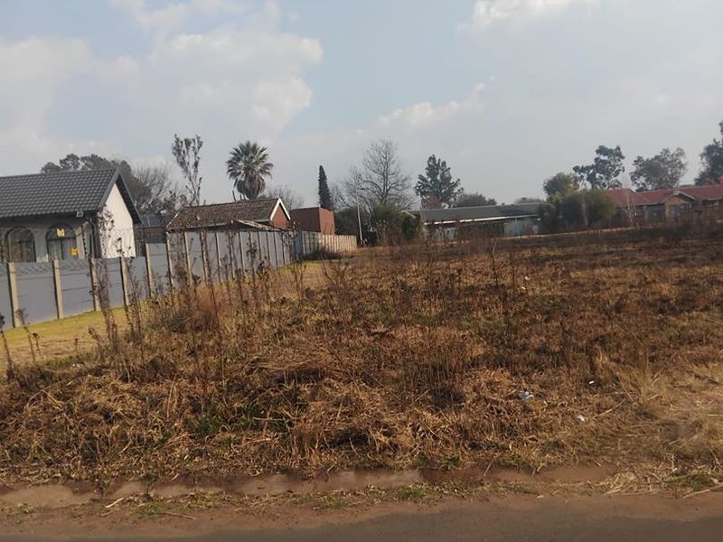 A vacant residential plot featuring a precast concrete boundary wall and direct access to a paved road.
