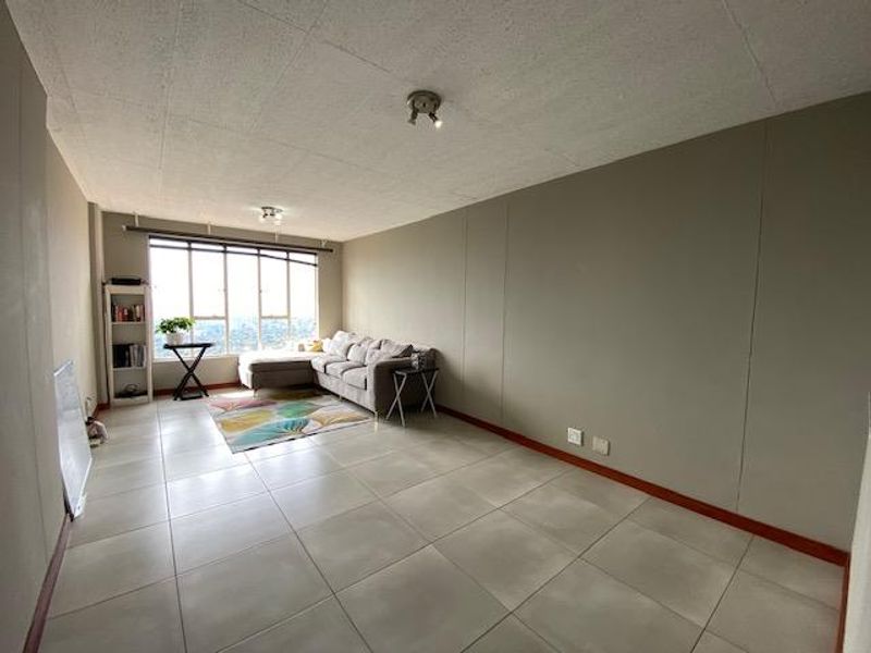 Spacious living room featuring large windows with natural light, neutral wall tones, and tiled flooring throughout.