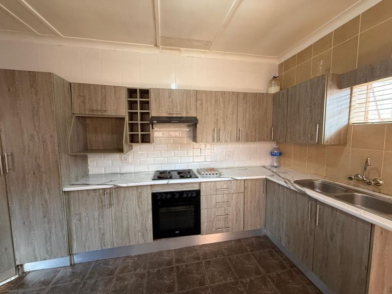 A functional kitchen featuring wood-look cabinetry, marble-effect countertops, built-in oven and hob, and tiled backsplash, offering a clean and practical workspace.