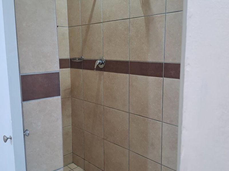 A functional shower enclosure featuring neutral-toned wall tiles with a decorative accent band and a standard shower fixture.