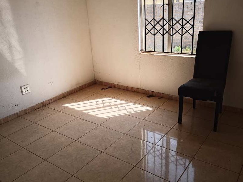 A vacant bedroom featuring tiled flooring and a window fitted with security bars, offering a blank canvas for potential interior design updates.