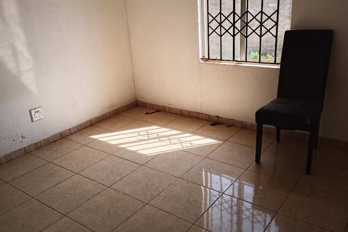 A vacant bedroom featuring tiled flooring and a window fitted with security bars, offering a blank canvas for potential interior design updates.