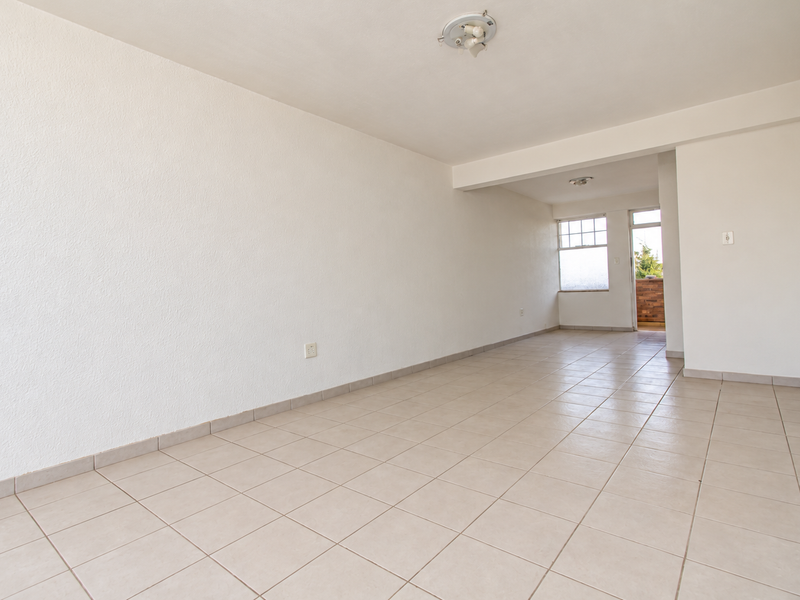 A spacious, empty living area featuring neutral ceramic tile flooring, textured walls, and direct access to an outdoor balcony space.
