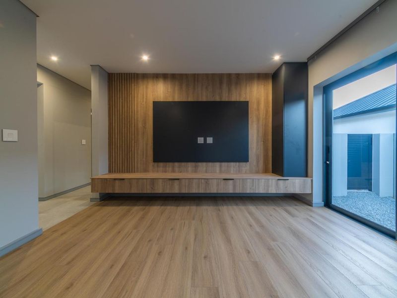 Modern living room featuring custom timber cabinetry, slat wall detailing, recessed lighting, and large sliding glass doors opening to an outdoor area.