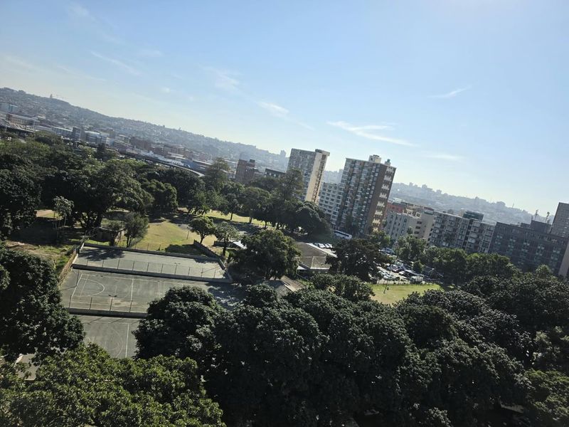 An elevated urban view overlooking a park area with sports courts and surrounding city buildings.