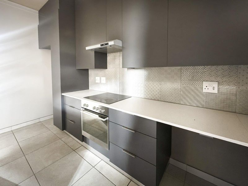 Modern kitchen featuring sleek dark grey cabinetry, stone countertops, integrated electric hob, oven, and extractor fan with a decorative tiled backsplash.