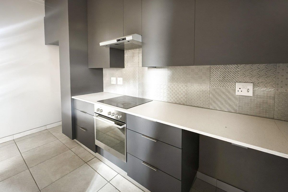 Modern kitchen featuring sleek dark grey cabinetry, stone countertops, integrated electric hob, oven, and extractor fan with a decorative tiled backsplash.