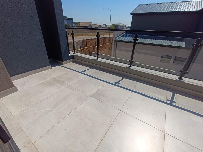 A modern, clean balcony featuring large format floor tiles and a contemporary glass balustrade with metal supports.