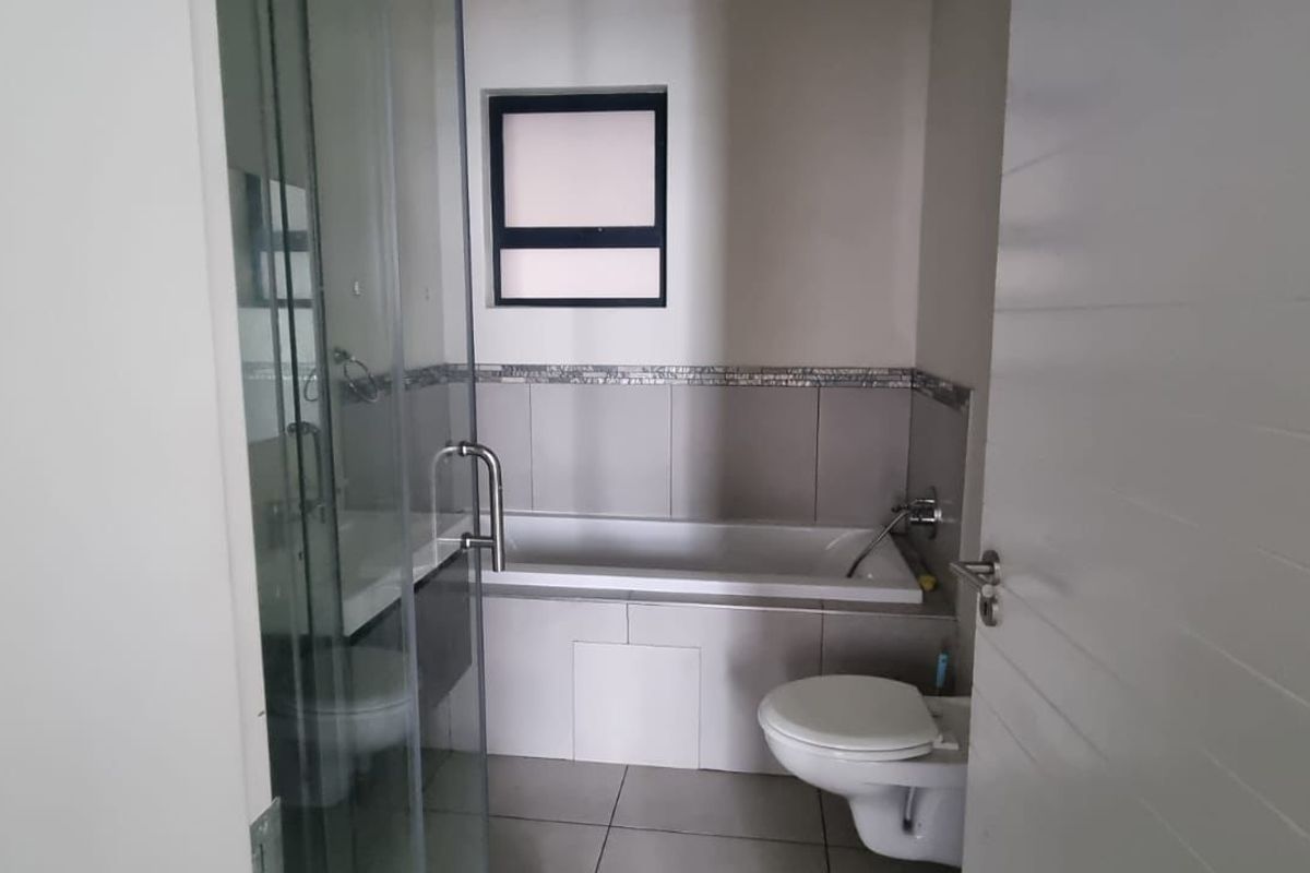 A modern bathroom featuring a built-in bathtub, a glass-enclosed shower, and a wall-mounted toilet with neutral tiling.