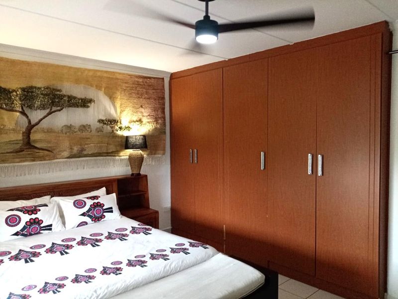 A bedroom featuring extensive built-in wooden cupboards and a modern ceiling fan, providing ample storage and climate control.