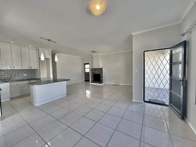 Spacious open-plan living area featuring a modern kitchen with island, tiled flooring, and a central fireplace, leading to an exterior security door.