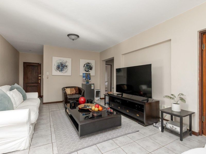 A comfortable living room featuring neutral wall tones, tiled flooring, and a functional layout with access to adjacent rooms.