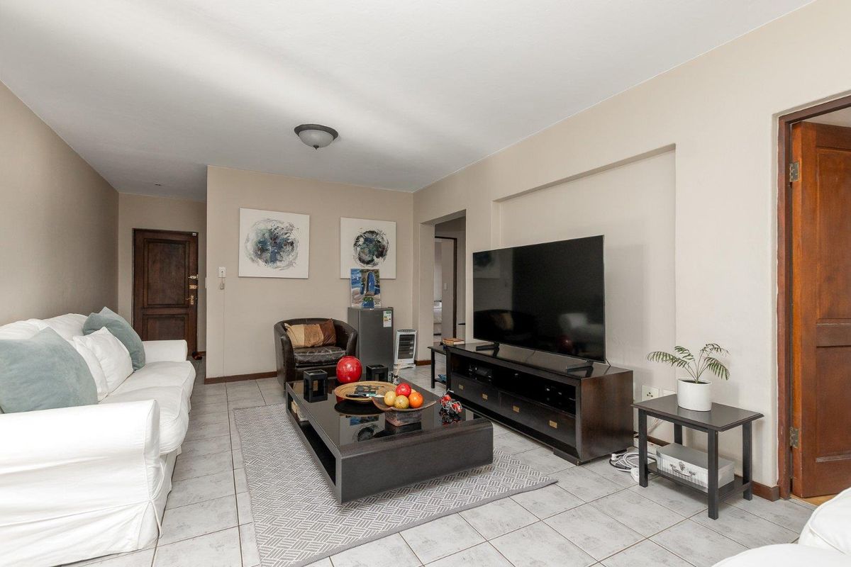 A comfortable living room featuring neutral wall tones, tiled flooring, and a functional layout with access to adjacent rooms.