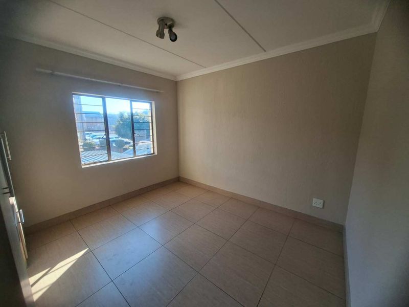 A vacant bedroom featuring neutral tiled flooring, a window with security bars, and a simple ceiling light fixture.