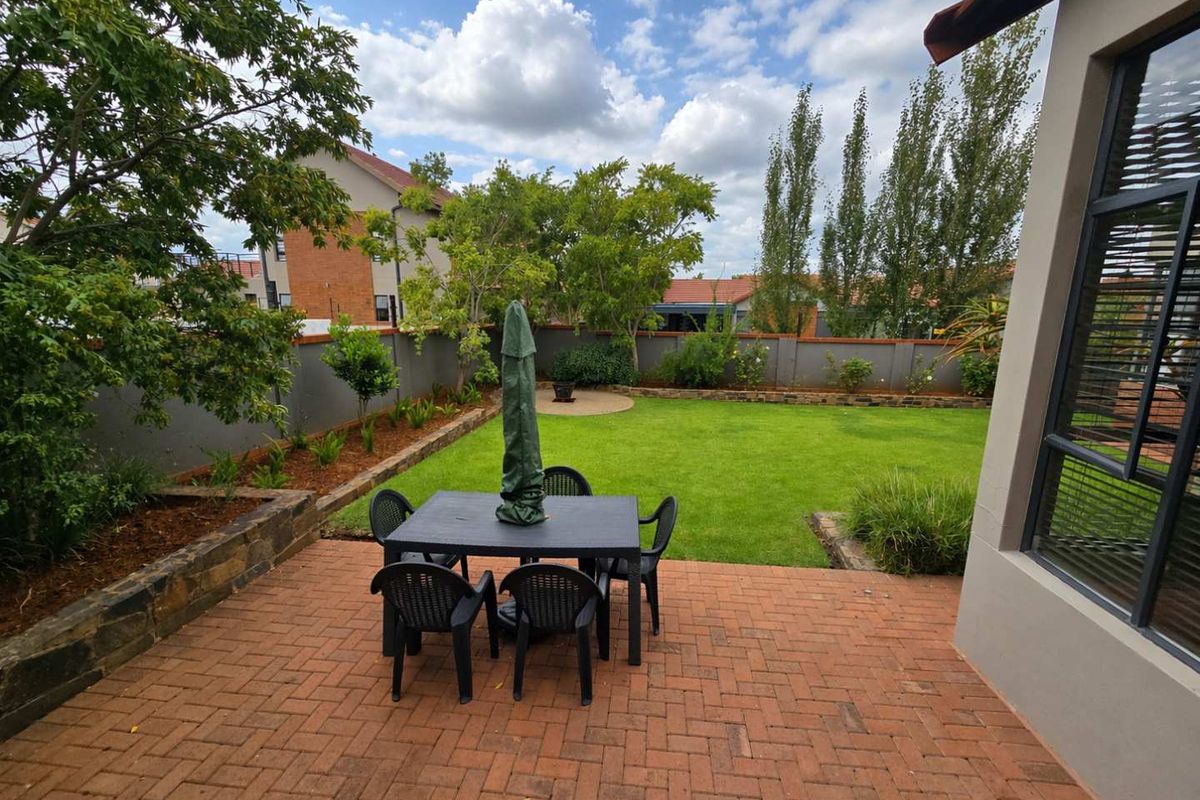 A private rear garden featuring a brick-paved patio area, a well-maintained lawn, and perimeter boundary walls.
