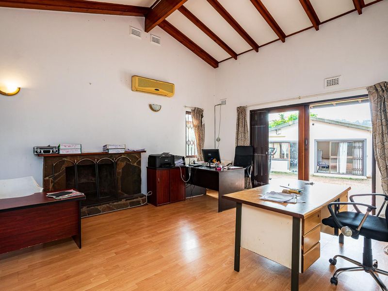 Spacious office featuring vaulted ceilings with exposed timber beams, a stone fireplace, and direct access to the outdoor area through sliding glass doors.
