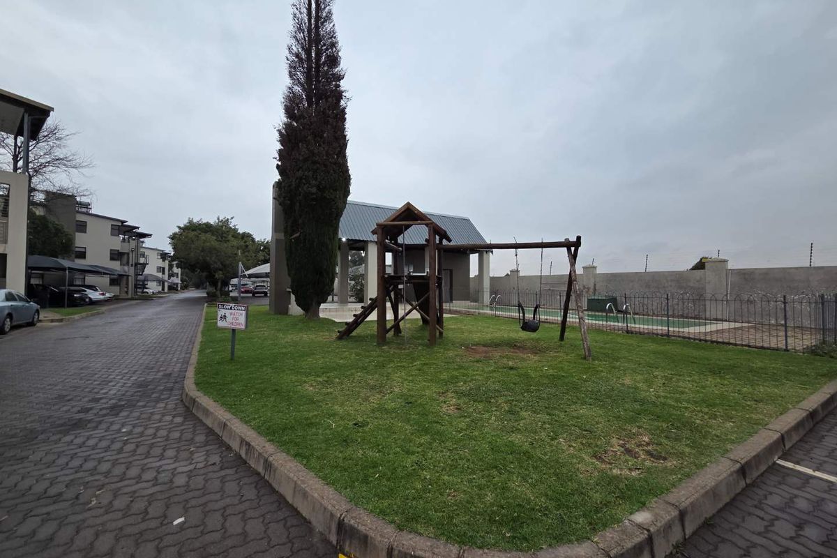 Communal outdoor area featuring a small playground, manicured lawn, and fenced swimming pool within the apartment complex grounds.