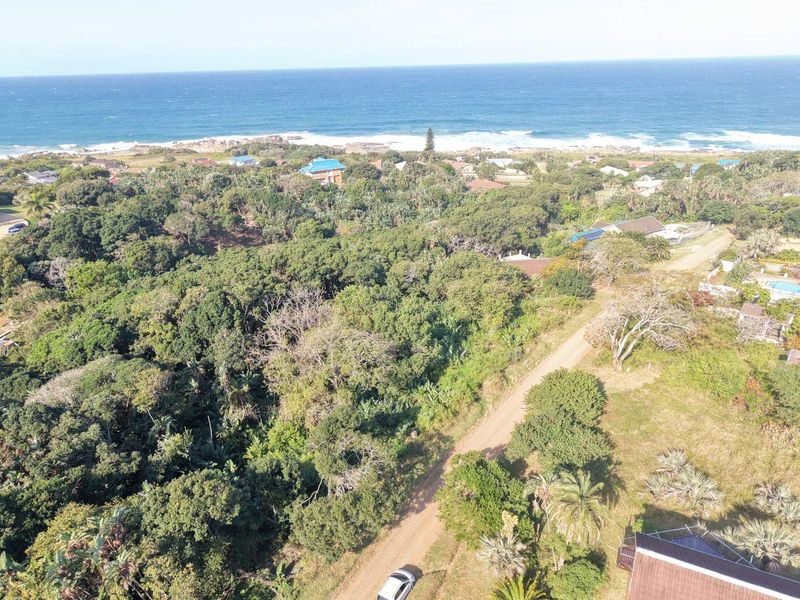 Aerial view of a coastal residential plot featuring dense natural vegetation and proximity to the ocean.