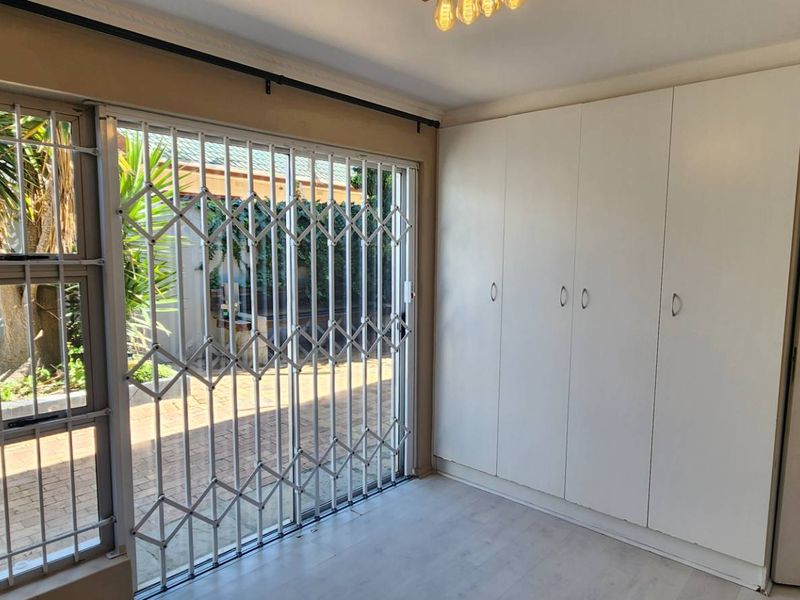 A bright, empty bedroom featuring built-in cupboards, laminate flooring, and a sliding door with a security gate leading to the exterior.