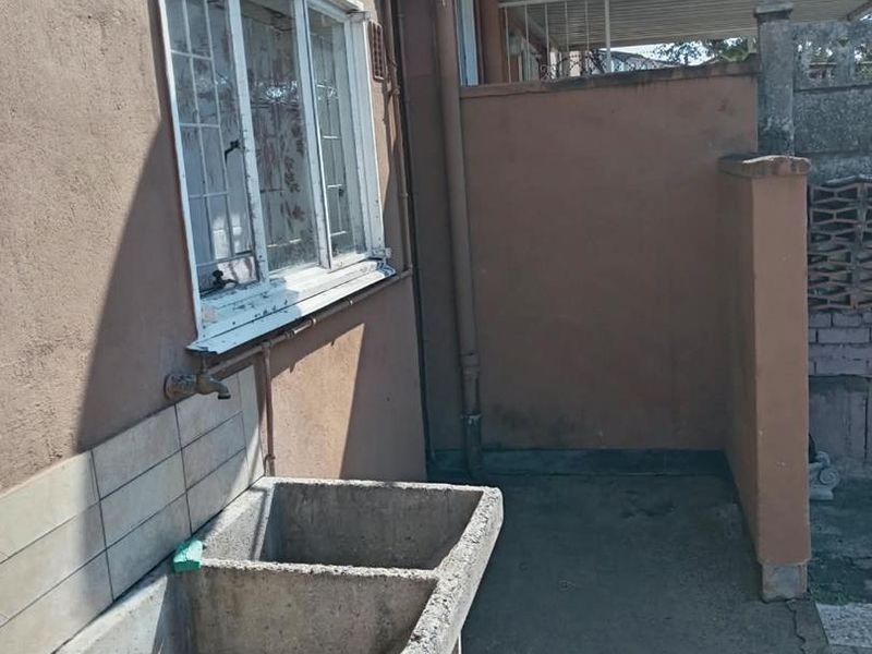 An outdoor laundry area featuring a concrete double trough, external tap, and tiled splashback, situated against the exterior wall of the townhouse.