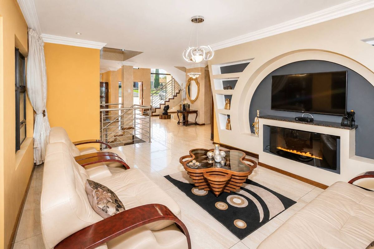 Spacious living room featuring a modern built-in fireplace, decorative recessed shelving, polished tile flooring, and an open-plan staircase with a stainless steel balustrade.