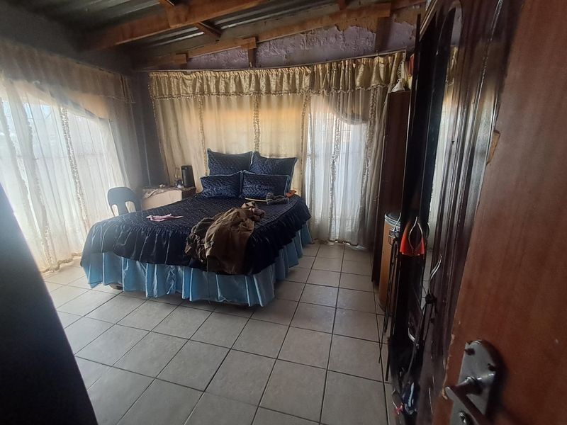 A bedroom featuring tiled flooring and exposed timber ceiling beams, currently requiring finishing work on the walls and ceiling.