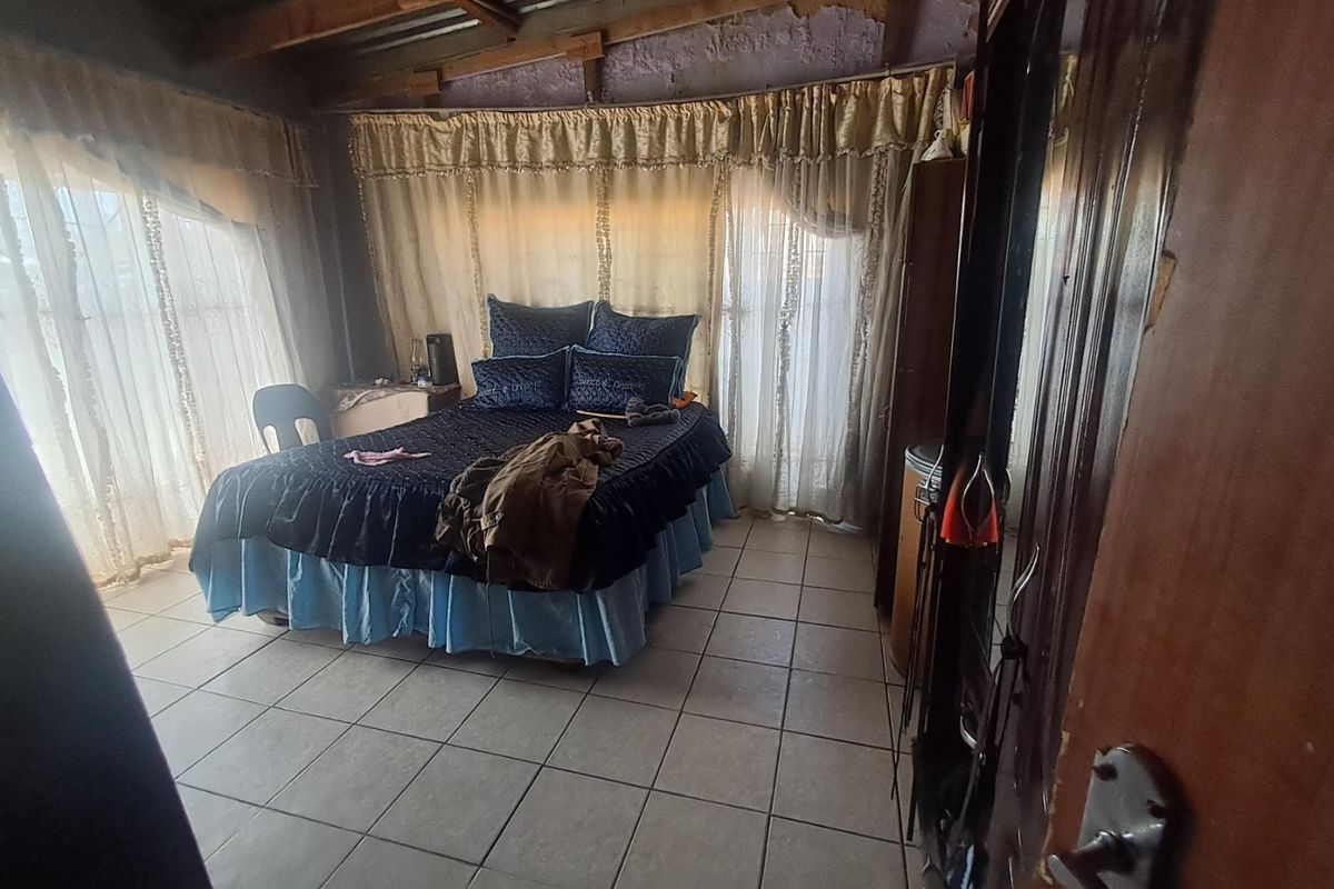 A bedroom featuring tiled flooring and exposed timber ceiling beams, currently requiring finishing work on the walls and ceiling.