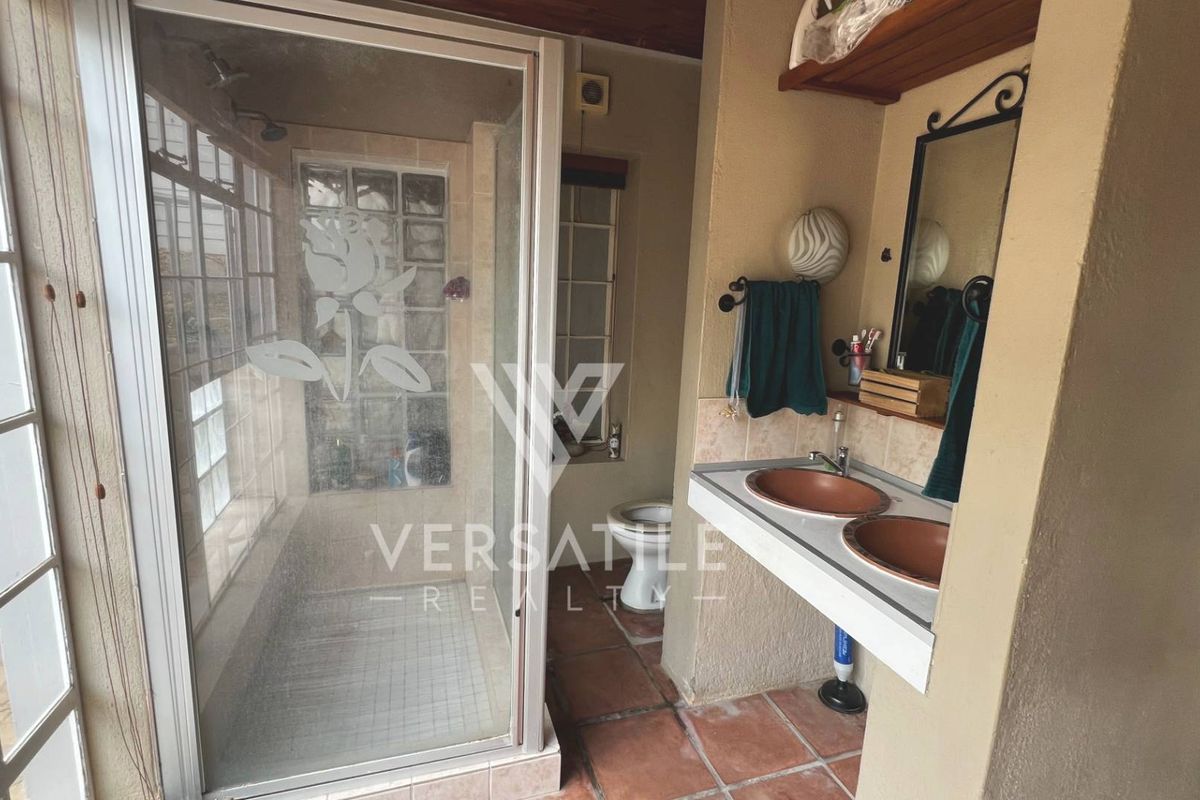 A dated bathroom featuring a glass-enclosed shower, dual vessel sinks on a built-in vanity, and terracotta-style floor tiles.