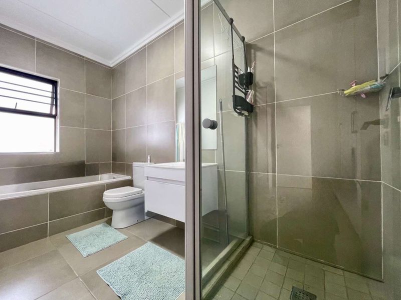 Modern bathroom featuring a built-in bathtub, a separate glass-enclosed shower, and a wall-mounted vanity with neutral floor-to-ceiling tiling.