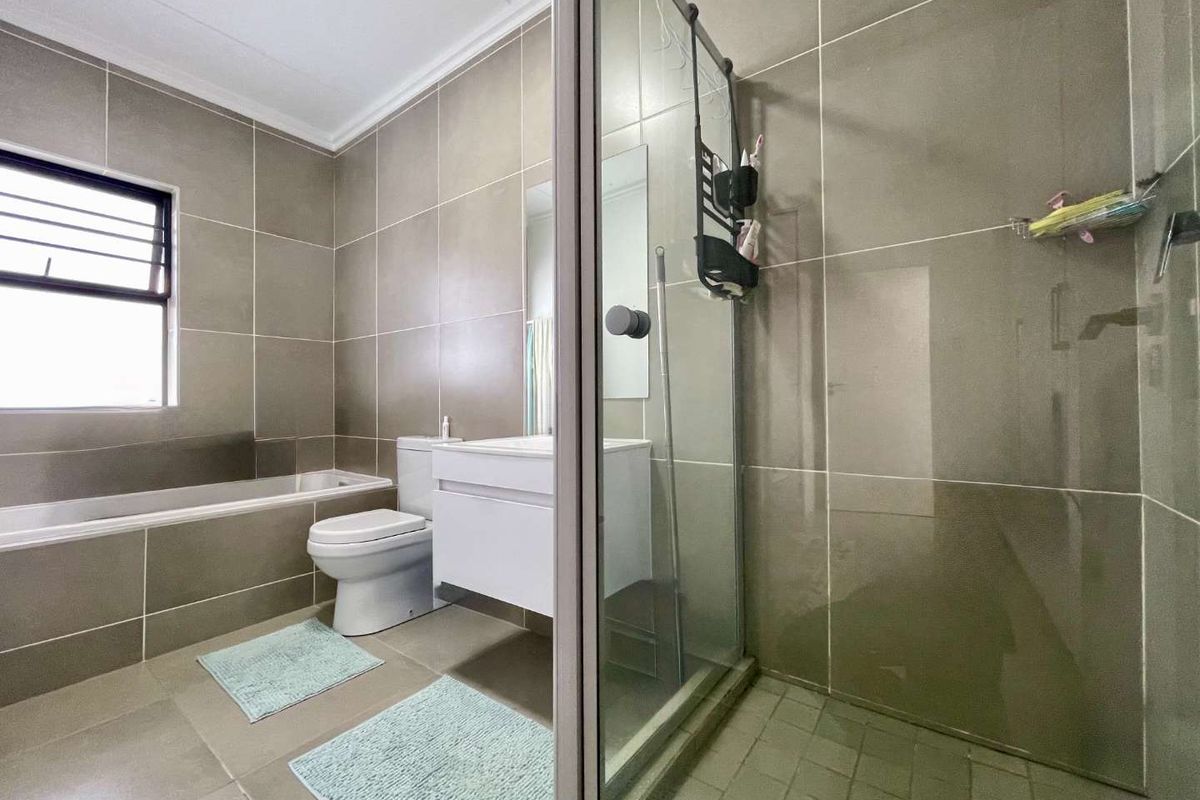 Modern bathroom featuring a built-in bathtub, a separate glass-enclosed shower, and a wall-mounted vanity with neutral floor-to-ceiling tiling.