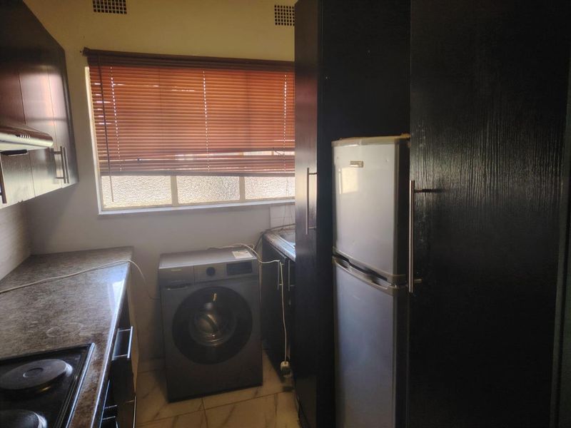 A functional kitchen featuring dark cabinetry, laminate countertops, a built-in hob with extractor fan, and a window with venetian blinds.