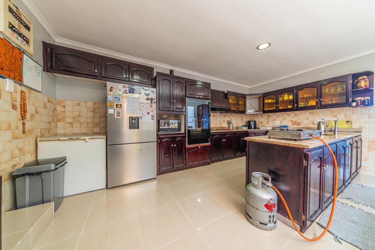 Spacious kitchen featuring dark wood cabinetry, granite countertops, a central island, and tiled flooring, offering ample storage and workspace.