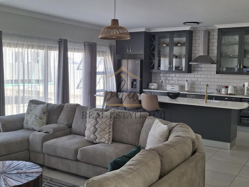 Modern open-plan living area featuring a contemporary kitchen with island, subway tile backsplash, and large sliding doors providing ample natural light.