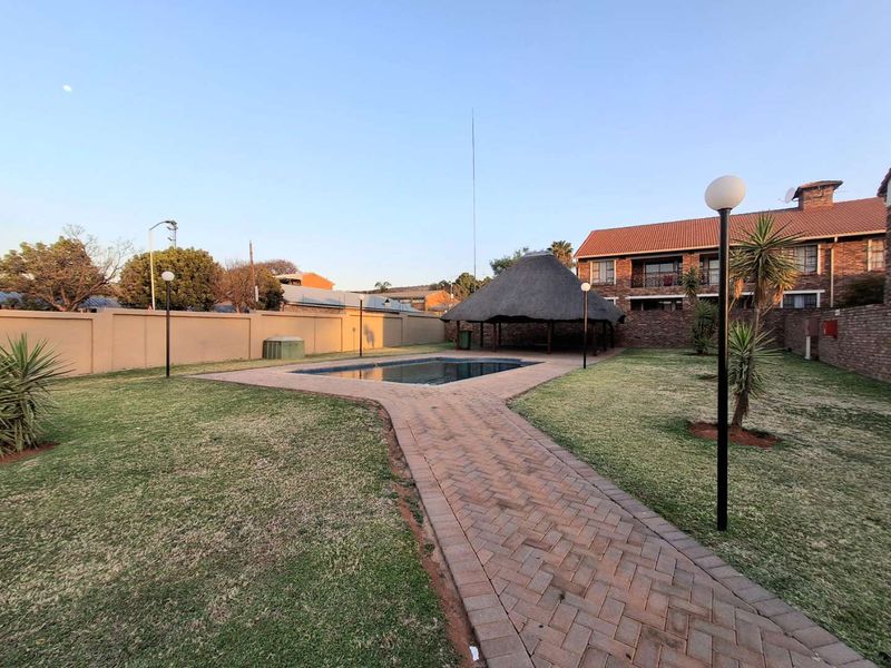 Communal outdoor area featuring a swimming pool, a thatch lapa for shade, and a paved walkway set within a landscaped garden.