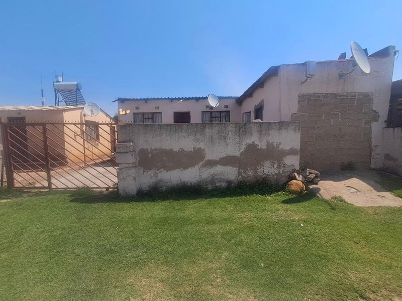 Rear view of the property featuring a lawn, boundary wall, metal gate, and solar water heating system installed on the roof.