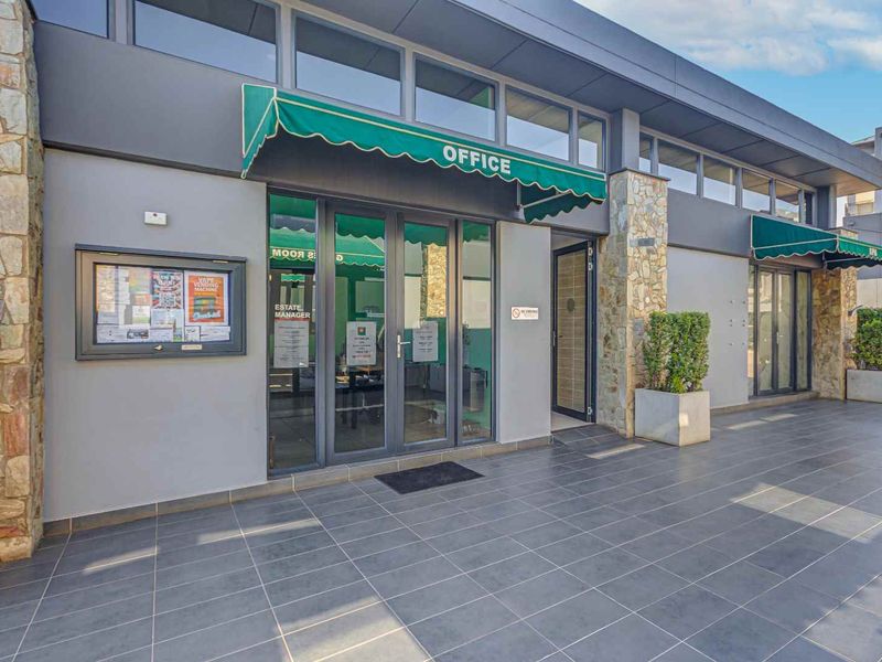 Exterior view of the apartment complex office entrance featuring tiled patio, stone cladding accents, and green fabric awnings over glass doors.