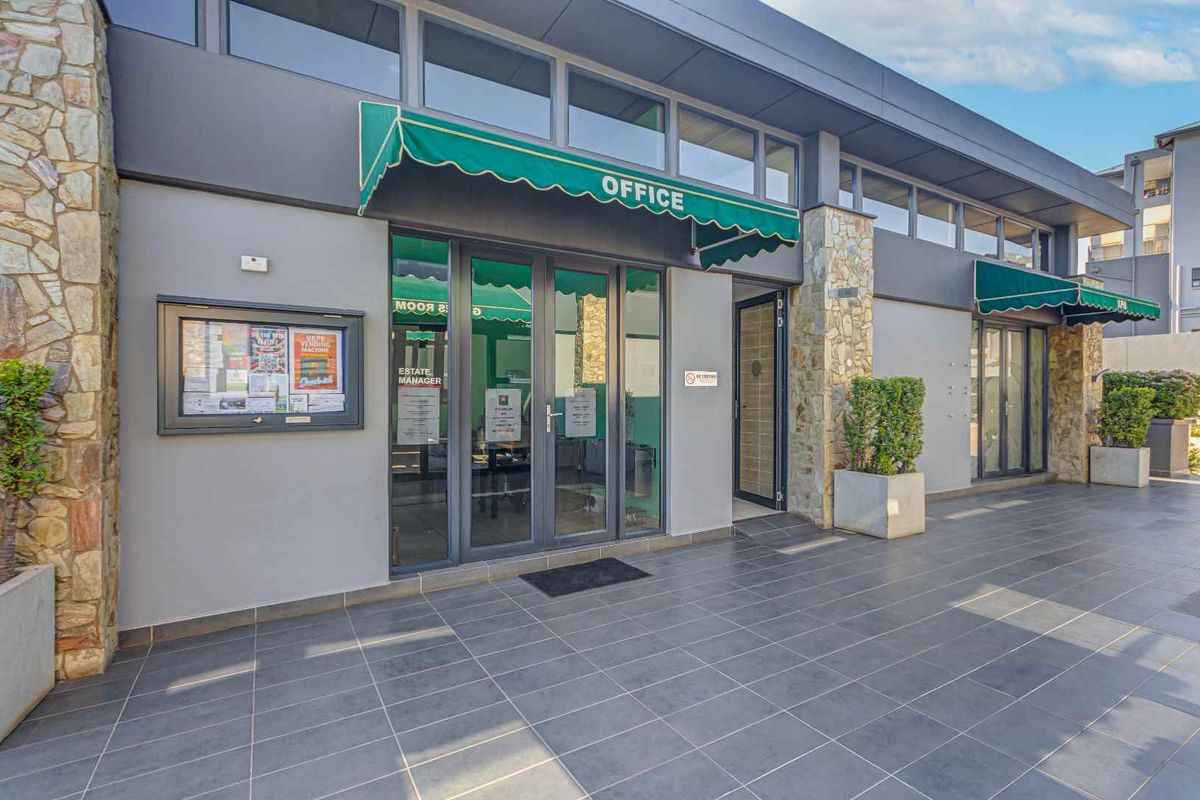 Exterior view of the apartment complex office entrance featuring tiled patio, stone cladding accents, and green fabric awnings over glass doors.