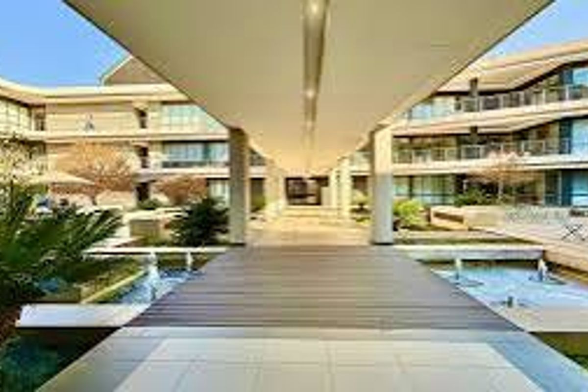 A modern office complex featuring a central covered walkway, landscaped gardens, and integrated water features between multi-story building wings.