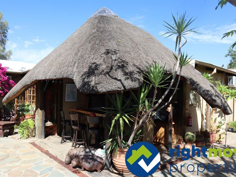 A charming outdoor entertainment area featuring a traditional thatched roof structure and a built-in bar, set on a stone-paved patio.