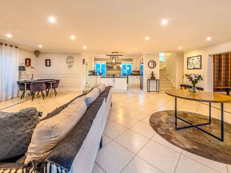 Spacious open-plan living area featuring tiled floors, recessed lighting, a modern kitchen with island, and a staircase leading to the upper level.