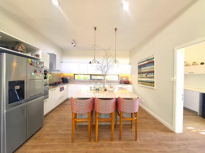Modern kitchen featuring a central island with stone countertops, sleek white cabinetry, integrated appliances, and warm under-cabinet lighting.