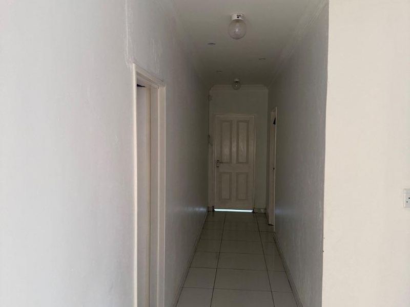A long, empty hallway featuring neutral tiled flooring, coved ceilings, and recessed lighting, providing access to multiple rooms within the property.