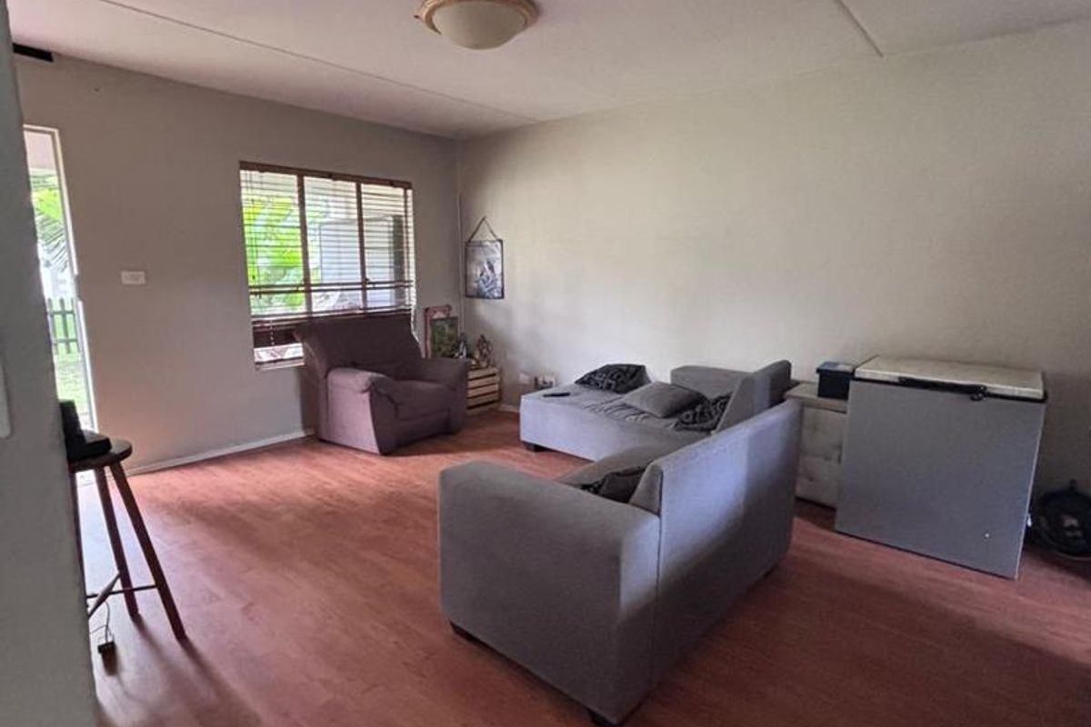 A spacious living area featuring wood-look laminate flooring, large windows for natural light, and a neutral color palette.