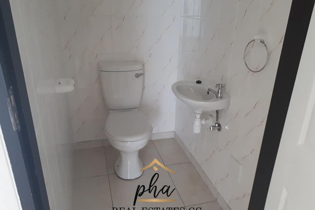 A compact guest bathroom featuring a white ceramic toilet, wall-mounted basin, and tiled walls.