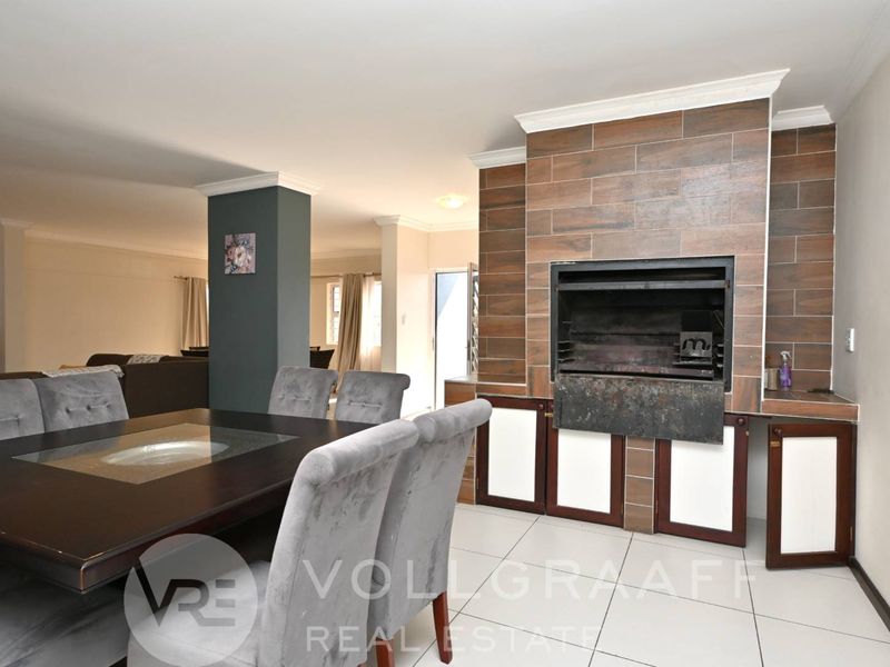 Open-plan living and dining area featuring a prominent built-in indoor braai with tiled surround and integrated cabinetry.