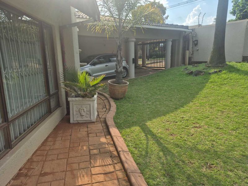 Front exterior view featuring a brick paved walkway, landscaped lawn, and a covered carport area with secure gated access.