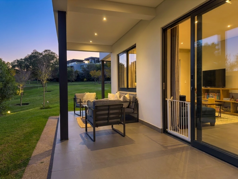 A modern covered patio featuring tiled flooring and recessed lighting, providing seamless indoor-outdoor flow through large sliding glass doors overlooking a landscaped garden.