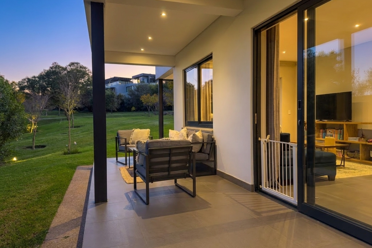 A modern covered patio featuring tiled flooring and recessed lighting, providing seamless indoor-outdoor flow through large sliding glass doors overlooking a landscaped garden.